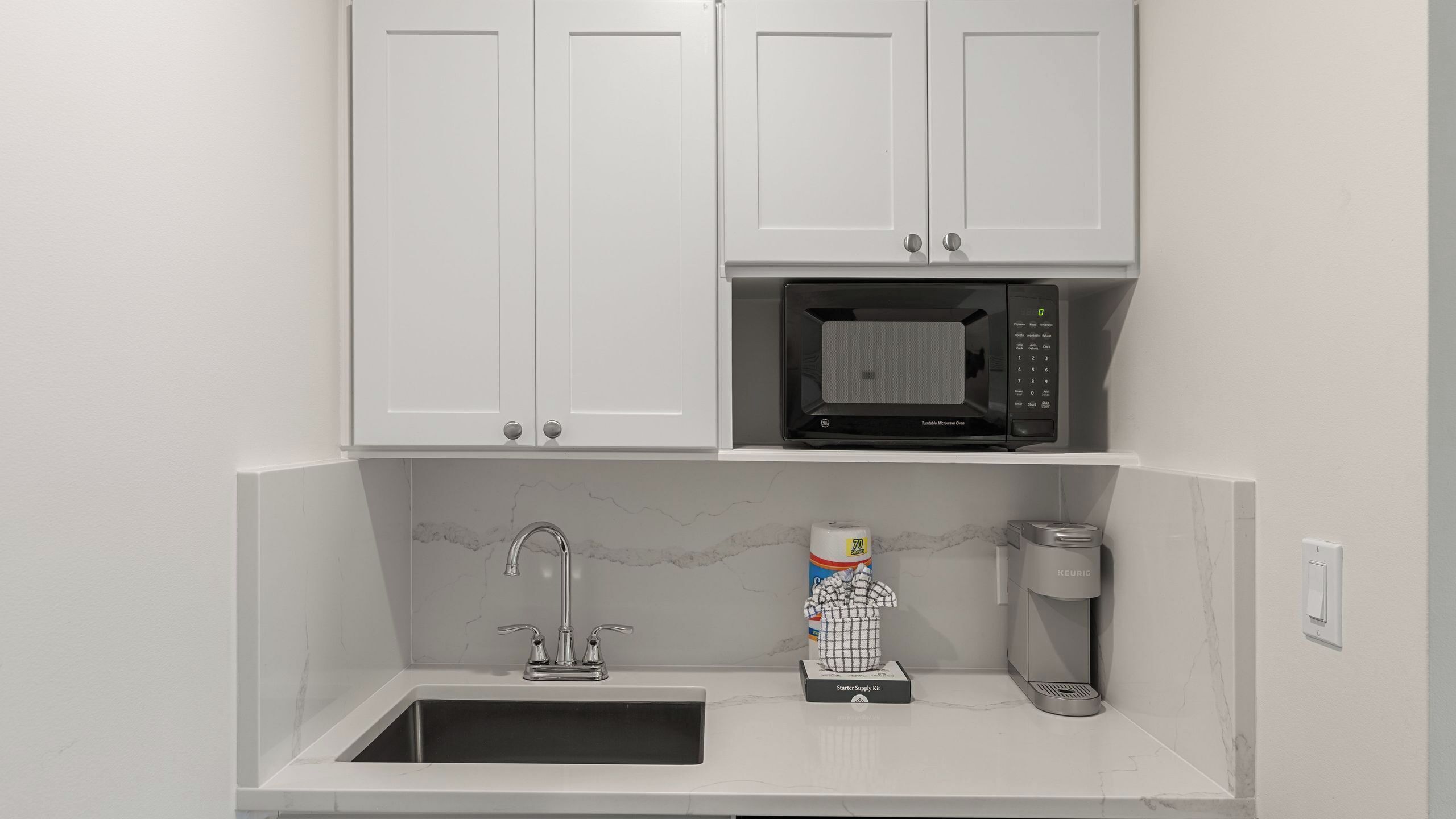 A kitchen with white cabinets, a built-in microwave, a sink, and a coffee maker.