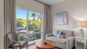 A room with a large window, a sofa, a chair, a coffee table, a lamp, and a painting. - Resort Condo Steps to Beach Pool, Hot Tub, Tennis, Golf Sandestin, Miramar Beach (Miramar Beach)
