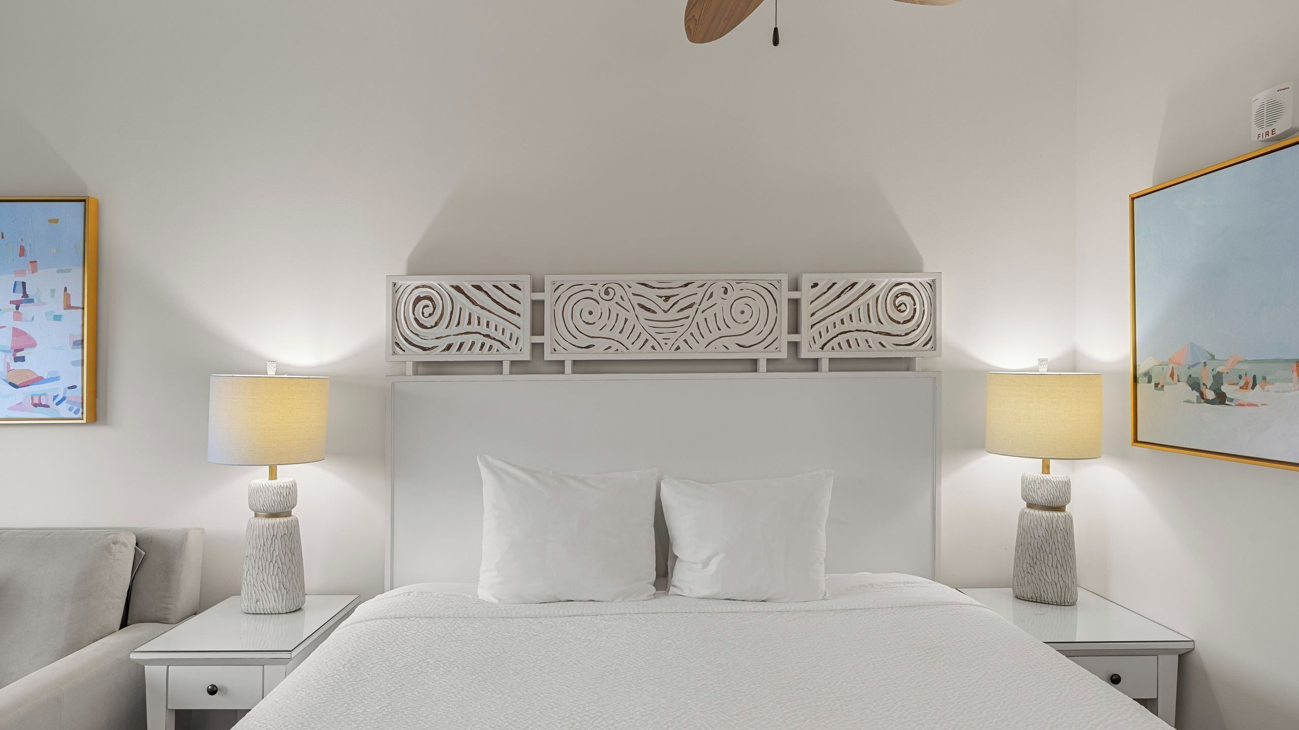Una camera d'albergo con un letto grande, due comodini con lampade, una ventola a soffitto e pannelli decorativi a parete.