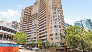 A high-rise building with multiple balconies, a visible ground-level bar, and a parking area. - Cozy Studio with Gym and Pool Near Chatswood Station (Liberty Grove)