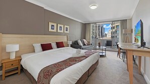 A hotel room with a large bed, a desk, a chair, a sofa, and a balcony with a city view. - Cozy Studio with Gym and Pool Near Chatswood Station (Liberty Grove)