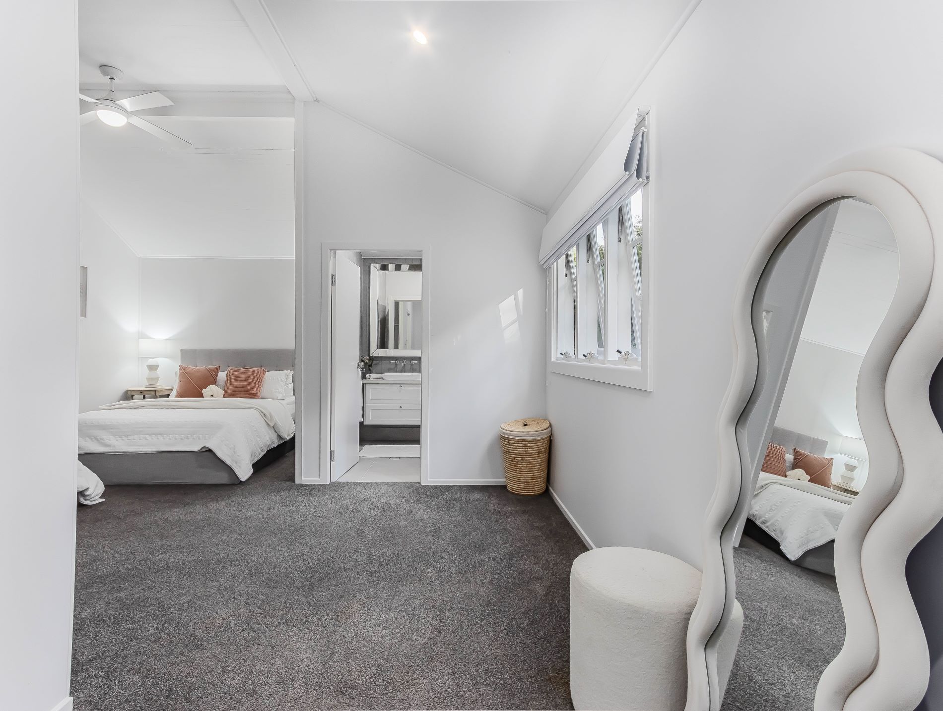 A modern bedroom with a bed, bedside table, mirror, and a window with curtains.