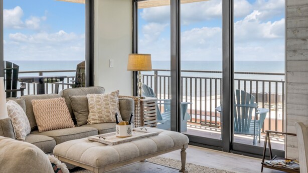 A balcony with a view of the ocean, furnished with a sofa, chairs, and a table.