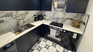 Een moderne keuken met donkere kastjes, een roestvrijstalen spoelbak, een zwart aanrechtblad en een marmeren achterwand.