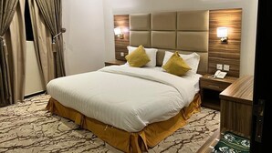 A hotel room with a large bed, a wooden headboard, two bedside tables with lamps, and a patterned carpet. - Dorrat Al-Mutamayzoon (Taif)