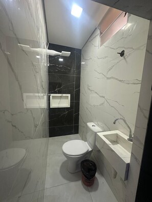 Et moderne badeværelse med toilet, bidet og vask, marmorvægge og bruseniche.