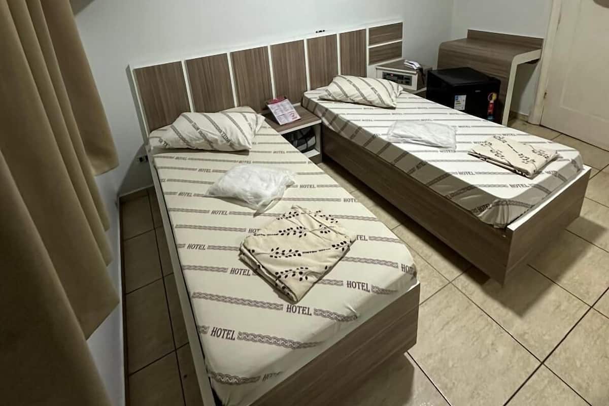 A hotel room with two beds, a small desk, a mirror, and a door.