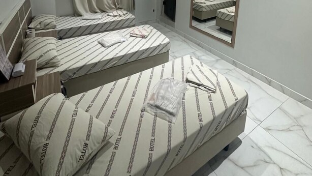 Habitación de hotel con tres camas, un televisor de pantalla plana montado en la pared y un espejo grande que refleja la habitación.