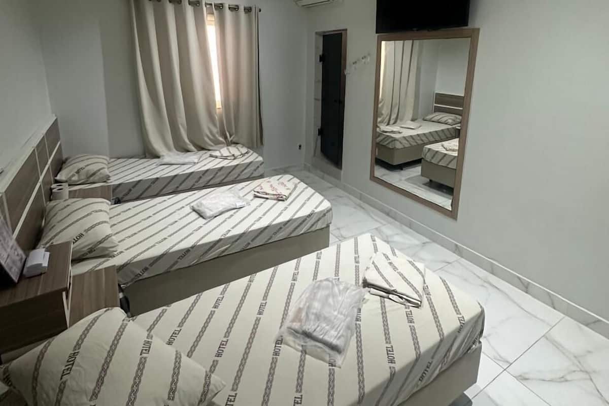 A hotel room with three beds, a flat-screen TV mounted on the wall, and a large mirror reflecting the room.