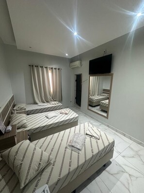 Une chambre d’hôtel avec trois lits, un téléviseur à écran plat fixé au mur et un grand miroir qui reflète la pièce.