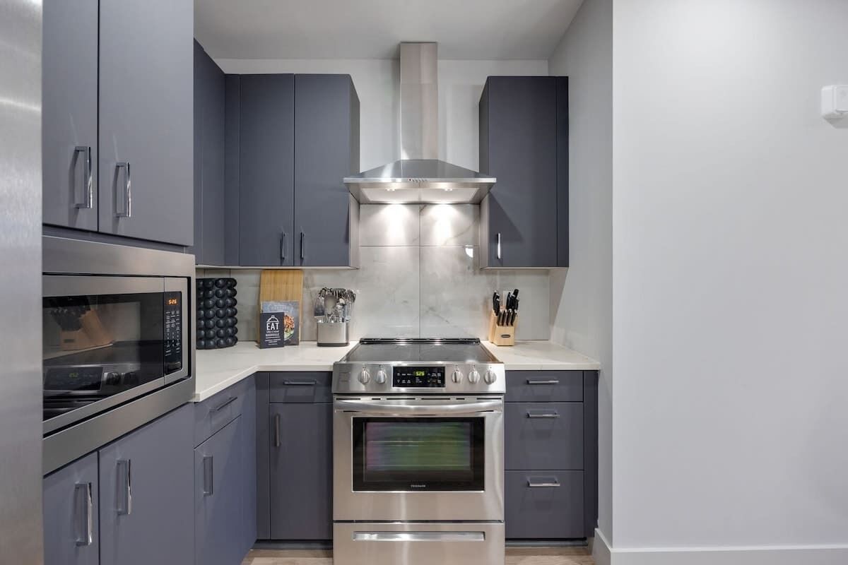 A modern kitchen with grey cabinets, a stainless steel range hood, a built-in oven, and a microwave.