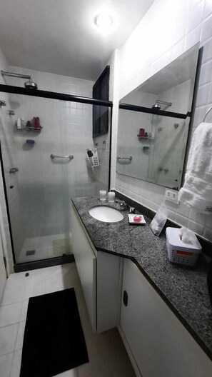 A modern bathroom with a glass-enclosed shower, a white sink, and a large mirror. - Hospeda Pluss (Rio de Janeiro)