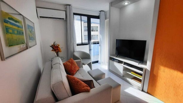 A modern living room with a sofa, TV, and a balcony with a view. - Hospeda Pluss (Rio de Janeiro)