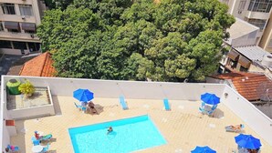 A rooftop pool area with a rectangular pool, surrounded by lounge chairs and umbrellas. - Hospeda Pluss (Rio de Janeiro)