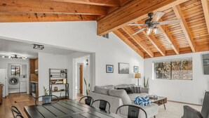 A modern living space with a dining area, kitchen, and a large window with a view of trees. - Tahoe Getaway near Kings Beach - Sleeps 9 (Kings Beach)