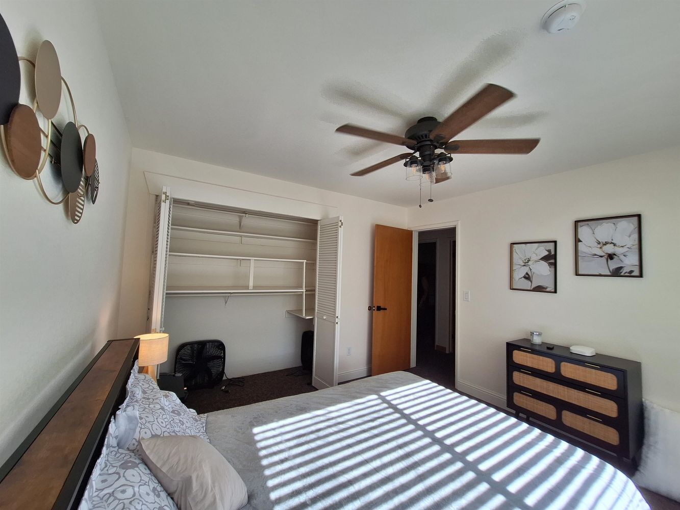 Une chambre à coucher comprenant un lit, un ventilateur de plafond, une armoire, un bureau et une chaise.