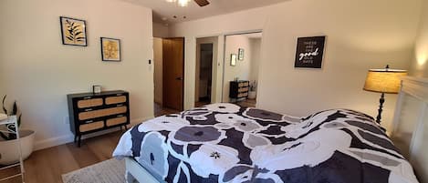 A bedroom with a bed, a ceiling fan, a dresser, a nightstand, and a wall with framed pictures.