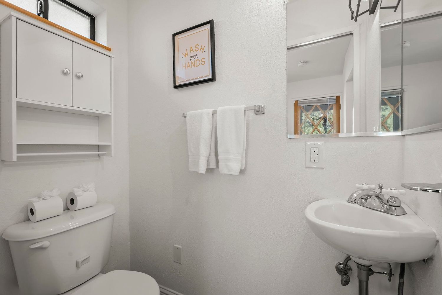 A bathroom with a toilet, a sink, a framed sign above the sink, and a towel rack with towels.