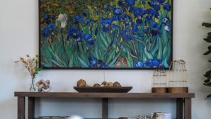 A living room with a wooden entertainment center, a large painting of blue flowers, and a vase with white flowers. - Charming 5-bedroom house in Cedarburg (Cedarburg)