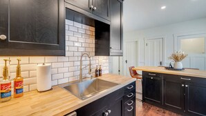 A modern kitchen with dark cabinets, a wooden countertop, a stainless steel sink, and a tiled backsplash. - Charming 5-bedroom house in Cedarburg (Cedarburg)