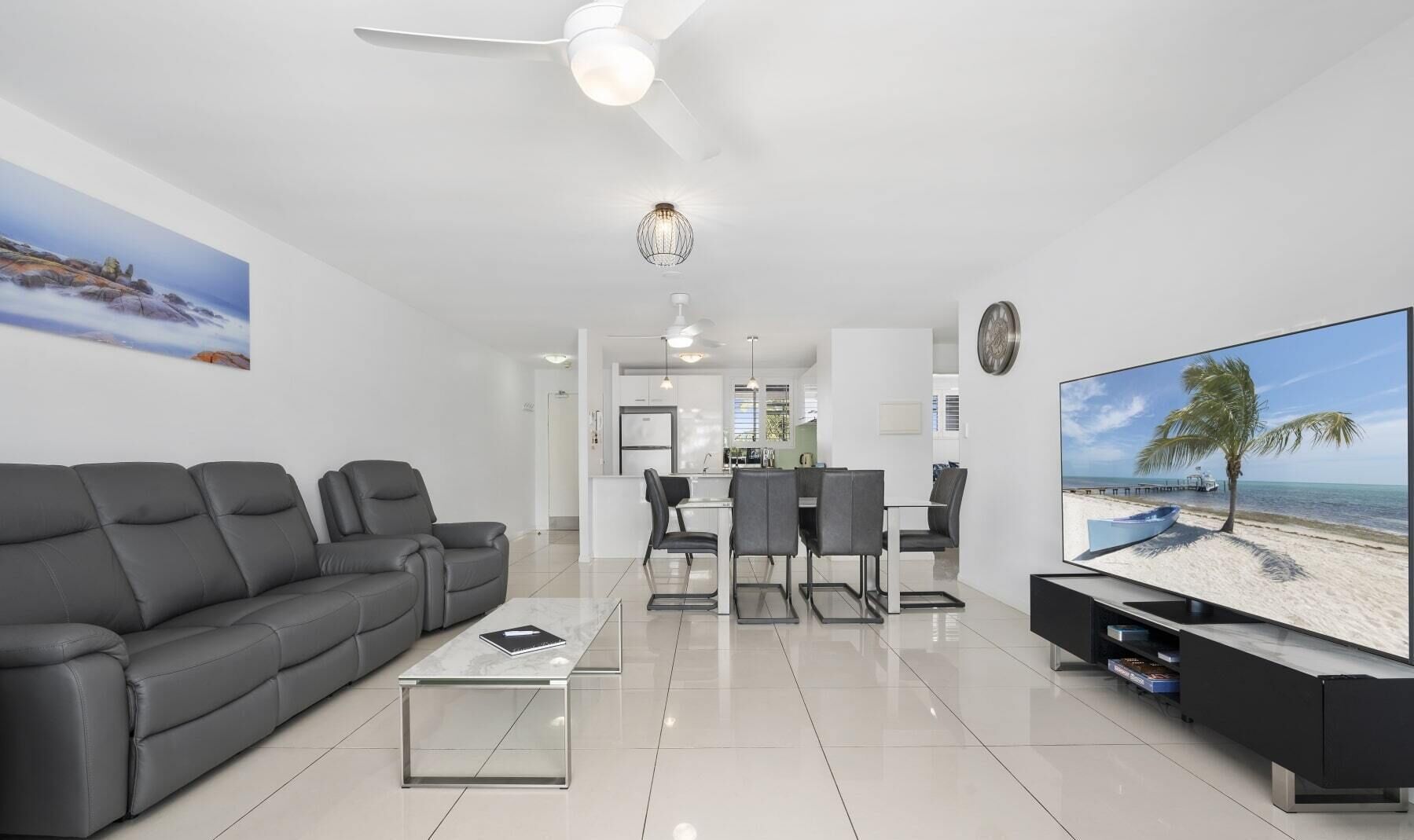 A modern living room with a grey sofa, a coffee table, a TV, and a dining area with chairs and a table.