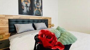 A bedroom with a wooden headboard, a bed with white bedding, a red flower, and a green throw.