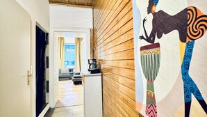 A hallway with wooden paneling, a white door, a small kitchenette, and a view into a living area with a sofa and curtains. - Spacious Studio for 4 Near FAC Platz (Vienna)