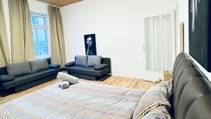 A modern bedroom with a large bed, a sofa, a small table, and a window with curtains. - Spacious Studio for 4 Near FAC Platz (Vienna)