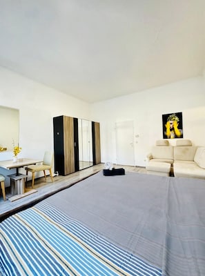 A modern hotel room with a bed, a sofa, a desk with a chair, a wardrobe, and a painting on the wall. - Nice Room in a Shared Apt, 10Min to FAC Platz (Vienna)