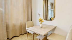 Ein Zimmer mit einem Holztisch, zwei Stühlen, einer Bank, einem Spiegel und einem Fenster mit Vorhängen.