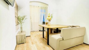 Ein modernes Wohnzimmer mit Holzboden, einer Couch, einem Esstisch und einem an der Wand befestigten Fernseher.