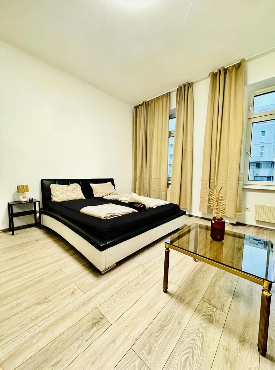 Une chambre moderne avec un lit noir et blanc, une table basse en verre et une vue sur les immeubles à travers de grandes fenêtres.
