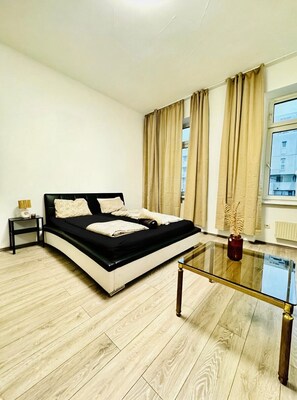 A modern bedroom with a black and white bed, a glass coffee table, and a view of buildings through large windows. - Comfy Room in a Shared Apt, Near FAC Platz (Vienna)