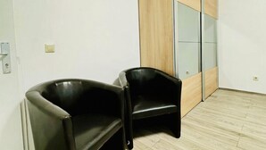 A room with a wooden floor, a black leather chair, and a wooden wardrobe with glass doors. - Comfy Room in a Shared Apt, Near FAC Platz (Vienna)