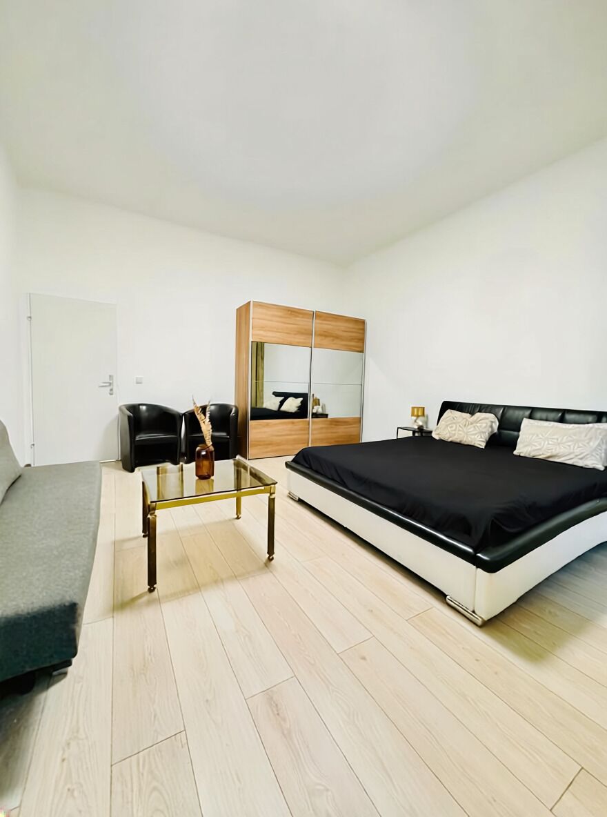 Un dormitorio moderno con cama, sofá, mesa de centro de vidrio, armario y espejo.