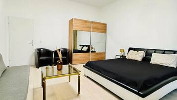 Un dormitorio moderno con cama, sofá, mesa de centro de vidrio, armario y espejo.