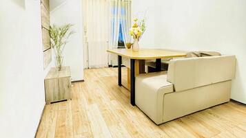 Una sala moderna con piso de madera, un sofá, una mesa de comedor y un televisor montado en la pared.