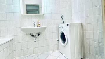 Un bany petit i net amb rajoles blanques, un lavabo, un mirall i una rentadora.