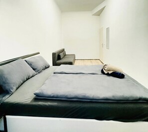 A minimalist hotel room with a bed, a sofa, and a door. - Cozy Room in a Shared Apt, 10Min to FAC Platz (Vienna)