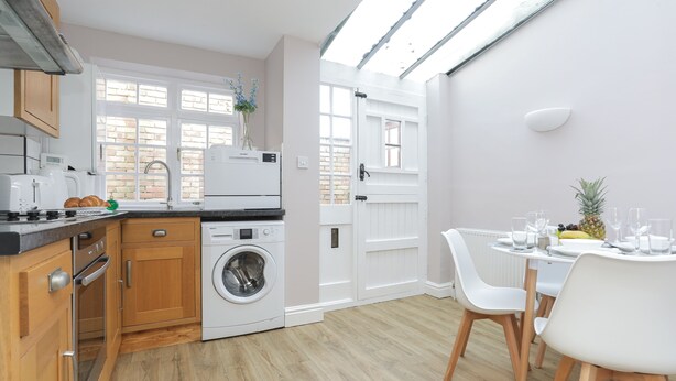 Une cuisine moderne avec des meubles en bois, un lave-linge encastré et un coin repas avec des chaises blanches et une table dressée pour deux personnes.