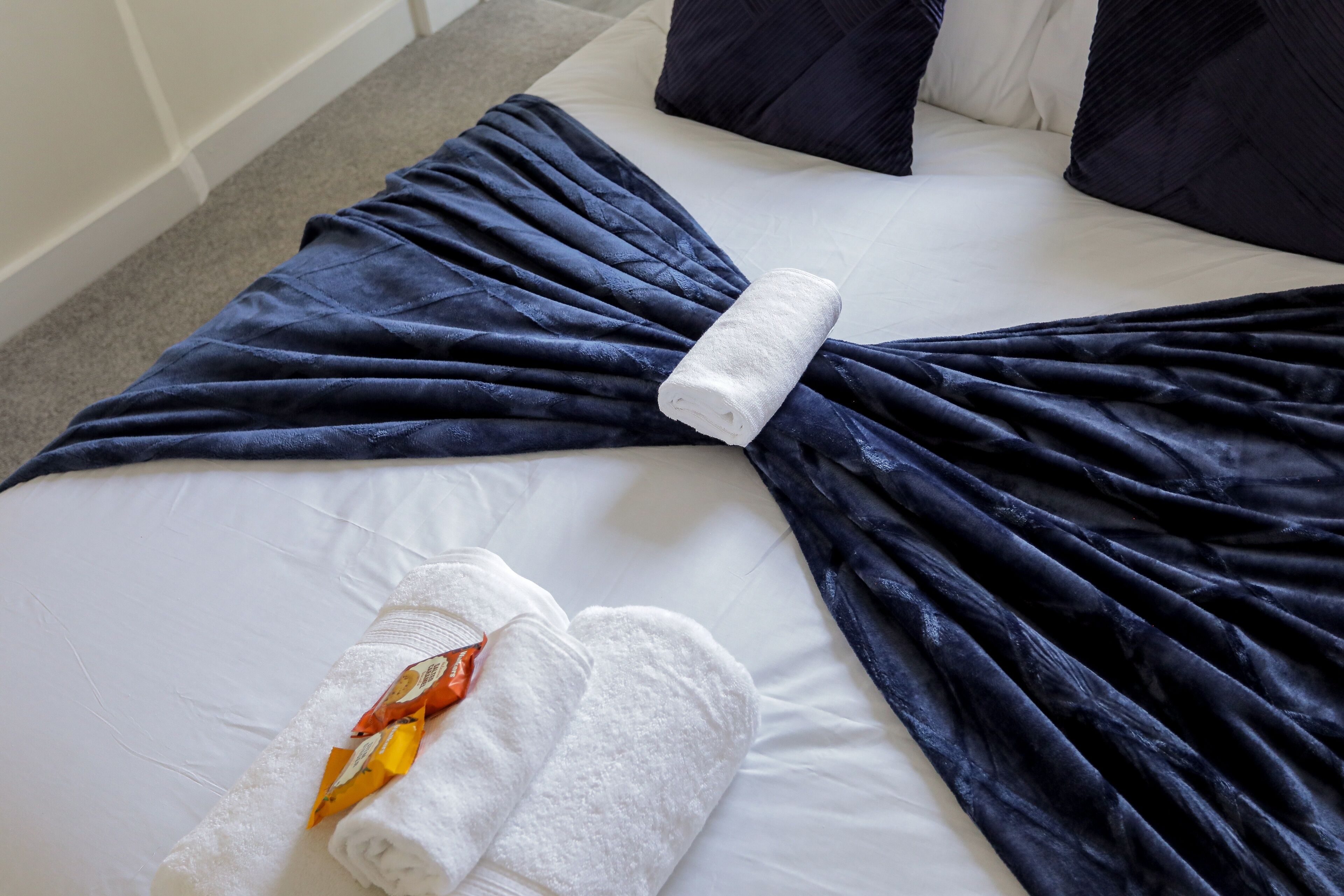 Ein ordentlich bezogenes Bett mit einer dunkelblauen Decke und einem weißen, gefalteten Handtuch.