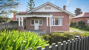 Een tweelaags bakstenen huis met een witte veranda en een voordeur.
