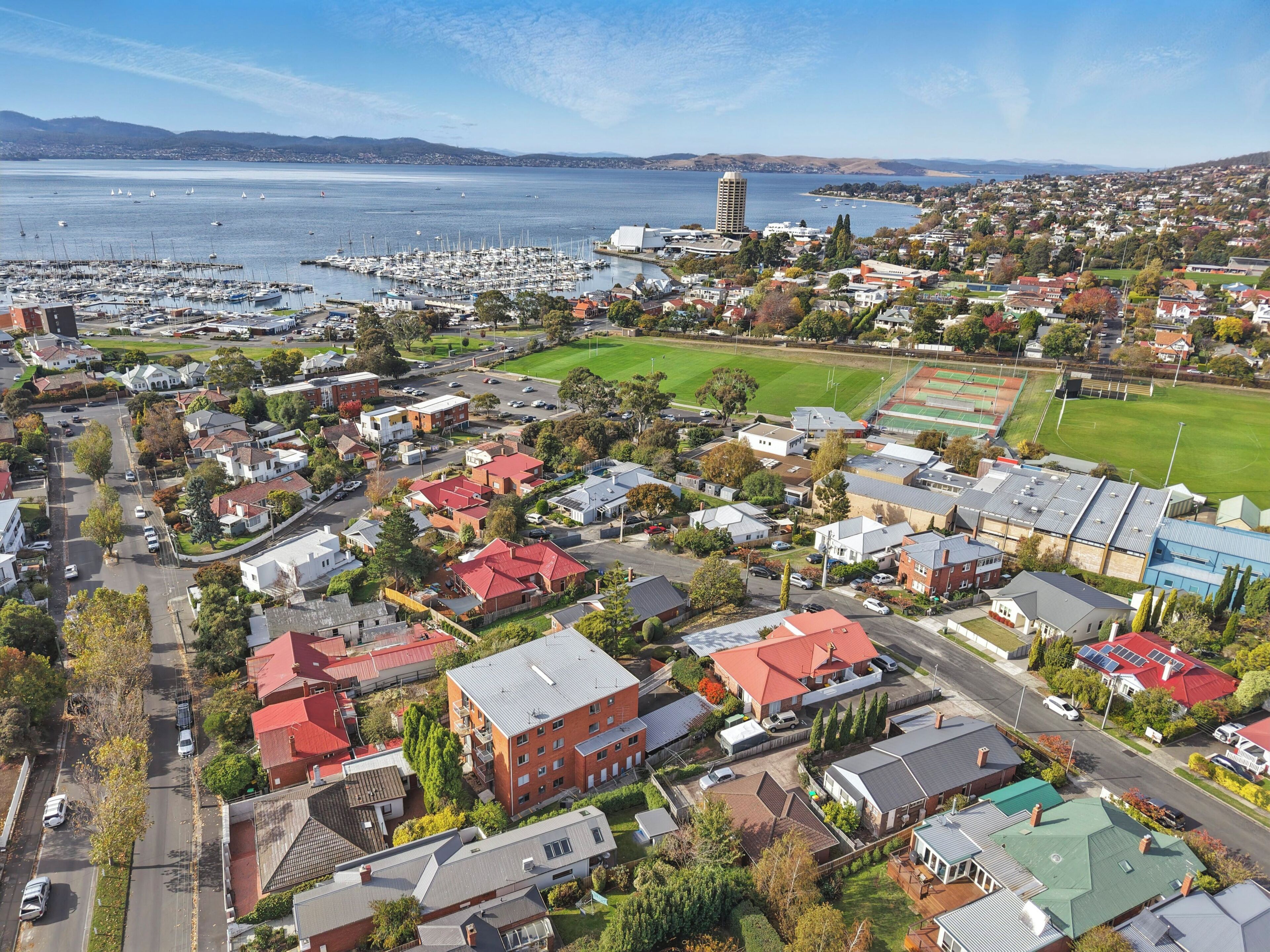 An aerial view of a coastal town with residential buildings, a marina, and a sports field.