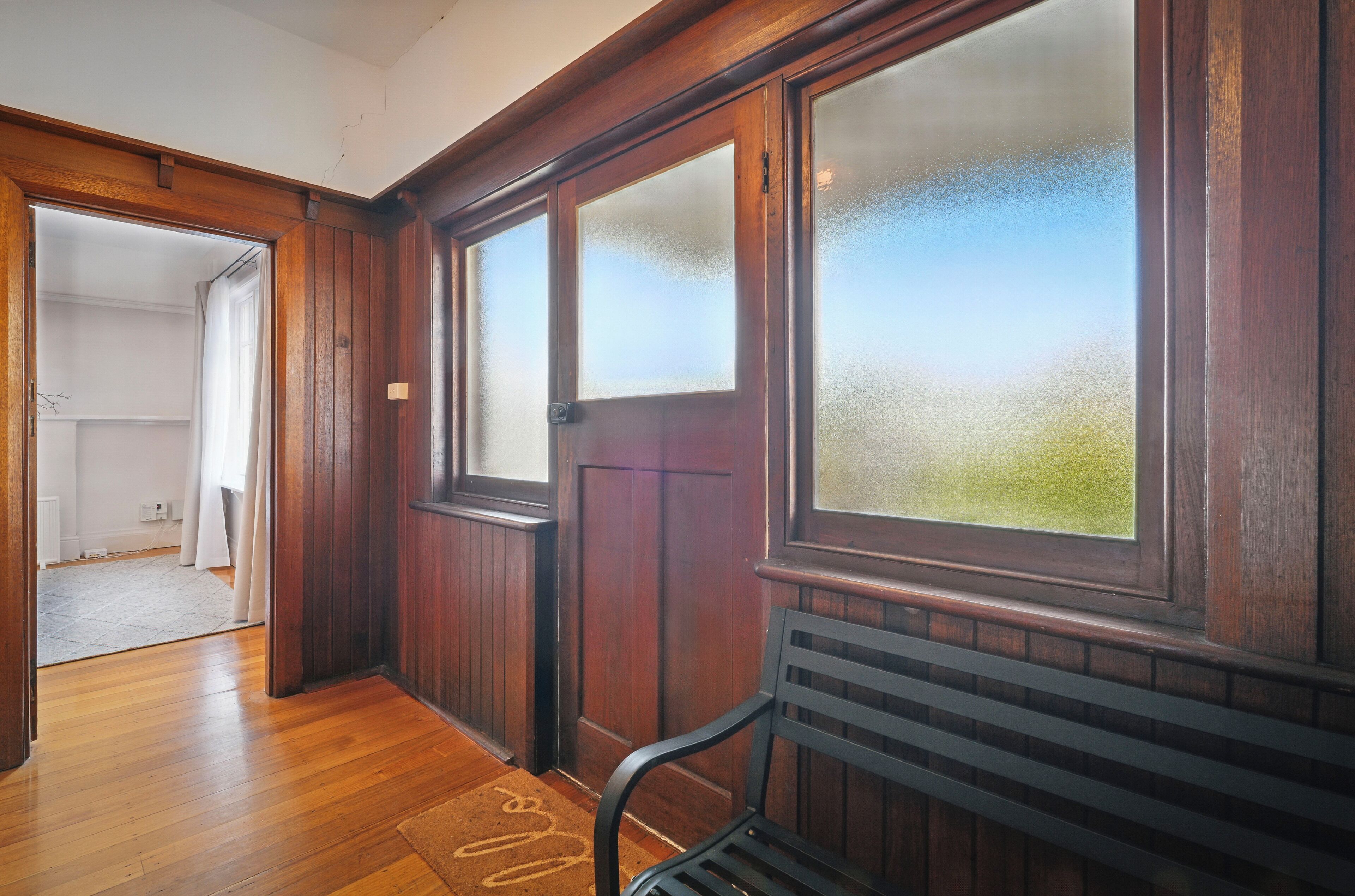 A hallway with wooden walls, frosted glass windows, and a bench.