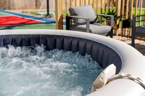 An inflatable hot tub with a dark interior and white exterior, surrounded by outdoor furniture and a wooden fence. - Near AT&T | Hot Tub • Pickleball • Sleeps 14 (Arlington)