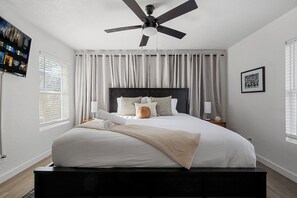 A modern bedroom with a large bed, a ceiling fan, and a TV on the wall.