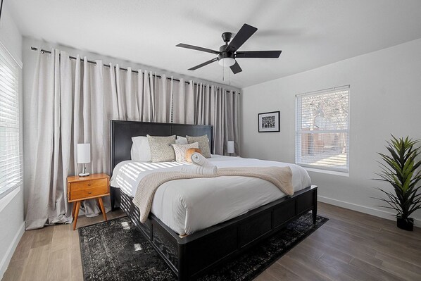 A bedroom with a bed, a nightstand, a ceiling fan, a window, and a plant.