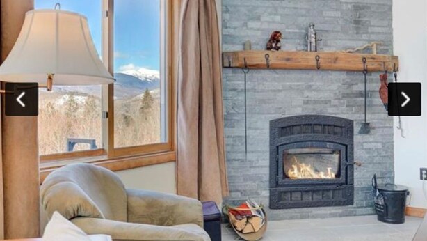 A cozy living room with a fireplace, a large window with curtains, and a comfortable sofa. - Amazing  2-bedroom condo above Story Land with AC, WiFi in beautiful Bartlett (Bartlett)