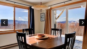 A dining area with a wooden table and chairs, large windows with a mountain view, and a hanging light fixture. - Amazing  2-bedroom condo above Story Land with AC, WiFi in beautiful Bartlett (Bartlett)