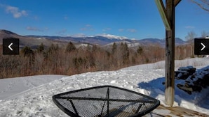 A snow-covered outdoor area with a metal chair and a wooden structure, overlooking a mountainous landscape. - Amazing  2-bedroom condo above Story Land with AC, WiFi in beautiful Bartlett (Bartlett)